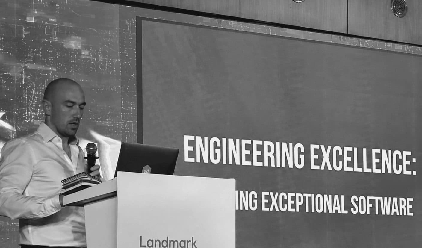Matthew D. Webb speaking from a lectern at Landmark Digital, beside a slide titled 'Engineering Excellence: Building Exceptional Software'.